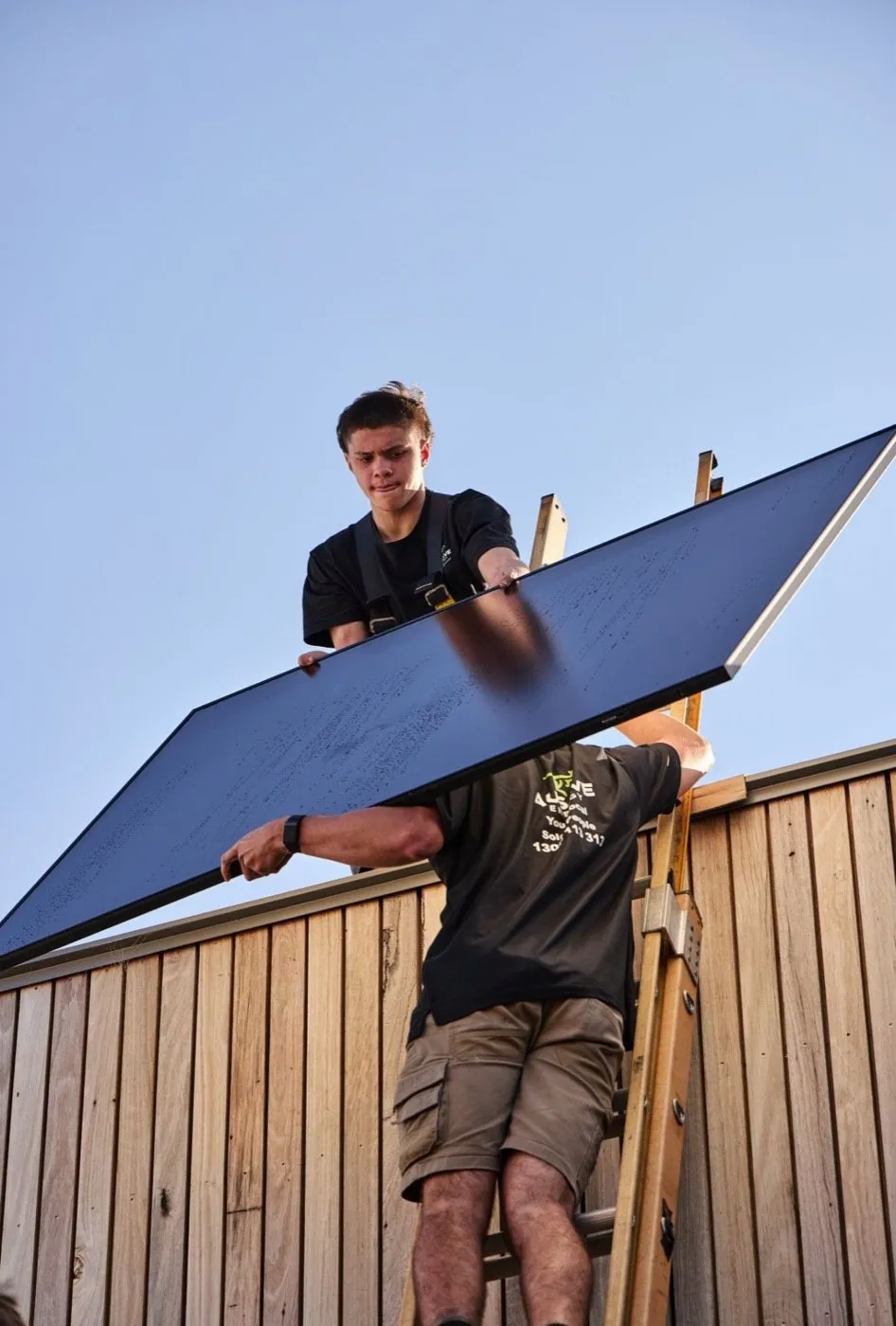Two Ausave installers lifting a panel onto a roof