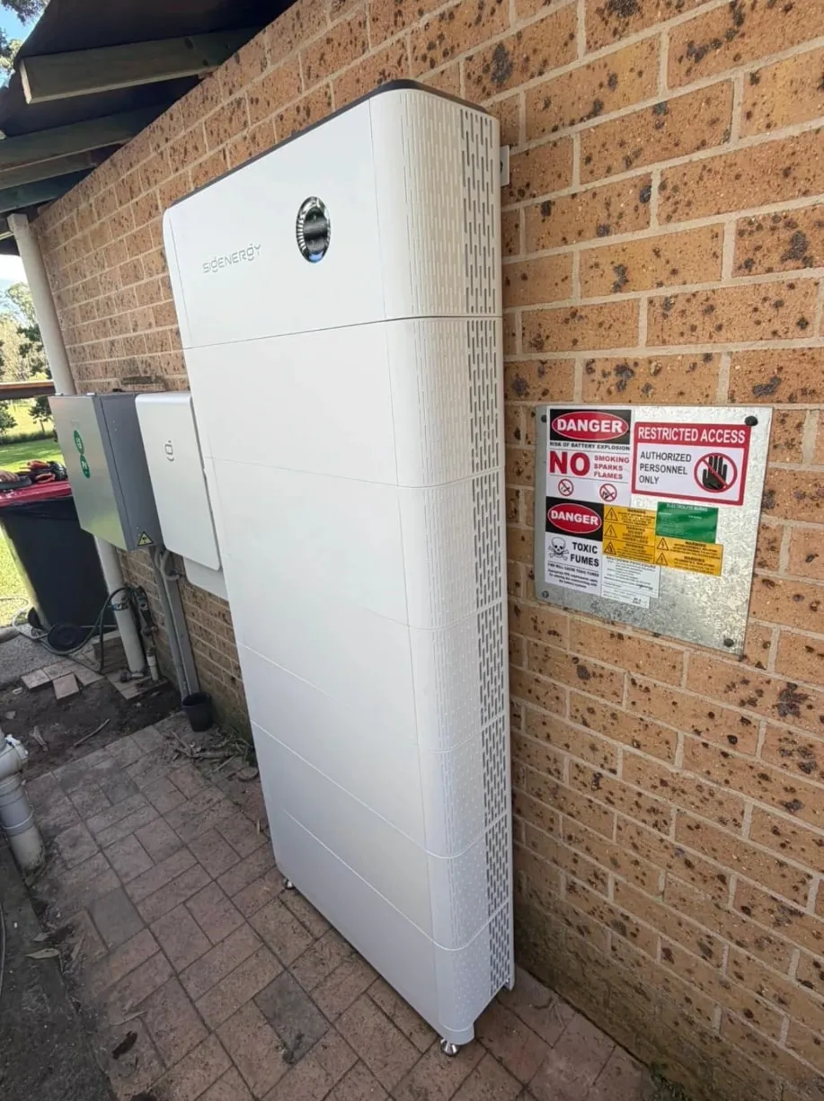 A full-height Sigenergy SigenStor stack outside against a brick wall, with a Sigen Energy Gateway on the wall beside it