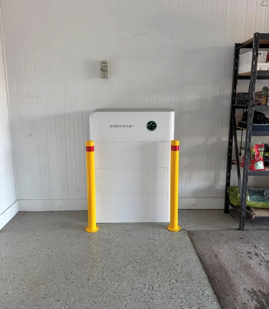 A Sigenergy SigenStor in a shed against white wall lining, with a yellow bollard either side