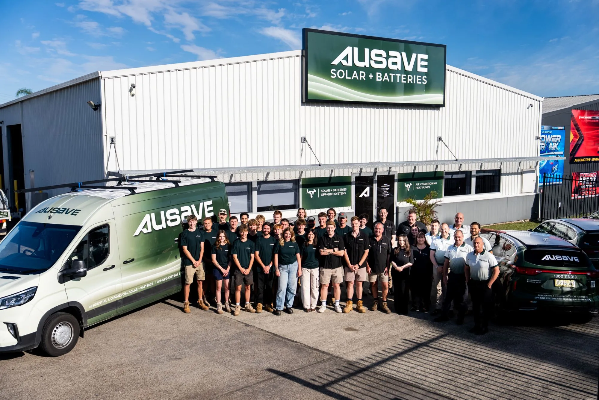 The Ausave team outside the Ausave Solar + Batteries building, beside an Ausave van and car
